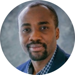 Professional headshot of a man wearing a blue checkered shirt against a gray background.