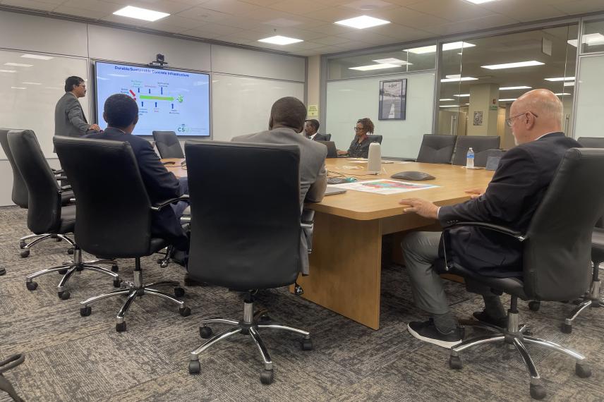 Business professionals seated around a conference table attending a presentation on sustainable concrete infrastructure displayed on a wall-mounted screen.