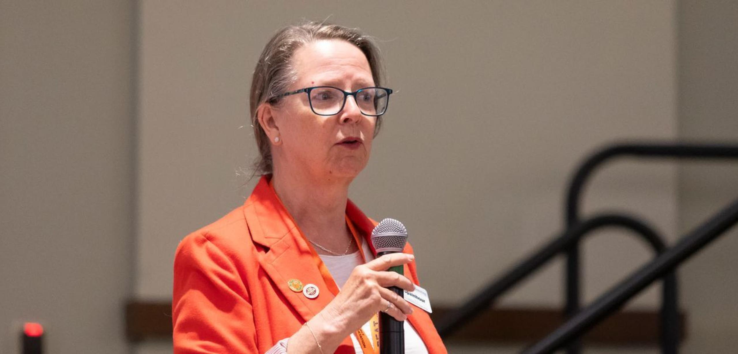 Woman is speaking at the front of a room holding a microphone