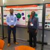 Two researchers present their research poster on transportation workforce development at an academic conference, standing in front of a detailed poster board display.
