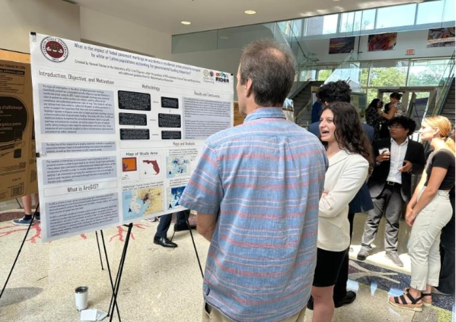 Two people standing in front of a poster board. They are talking to each other.